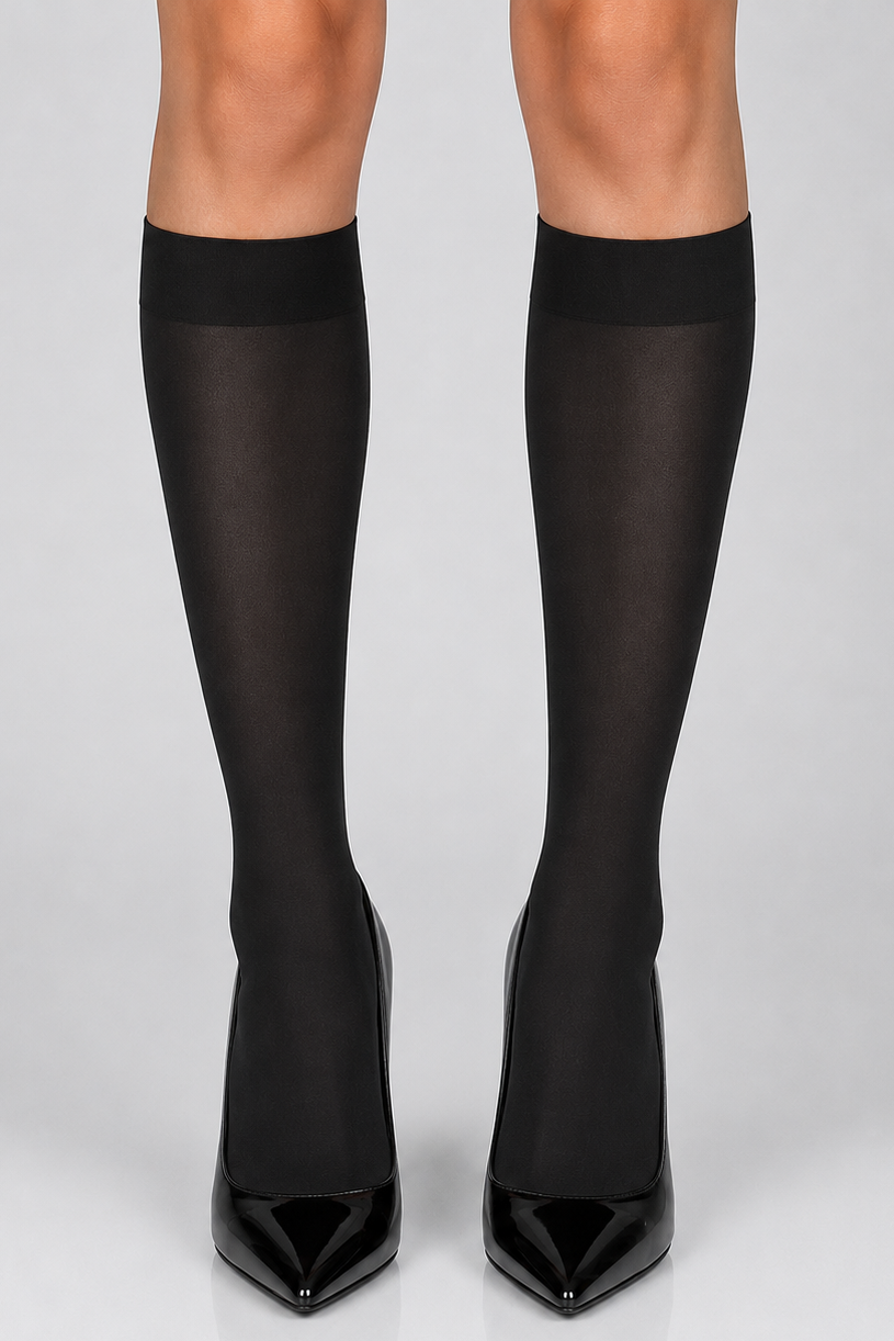 Black knee-high sheer tights worn with black pointed-toe high heels, shown on a model's legs against a light gray studio background.
