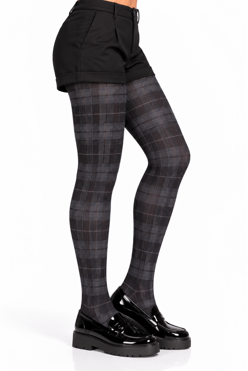 A person shown from the waist down wearing dark plaid tights, black shorts, and black patent leather loafers against a plain white studio background.