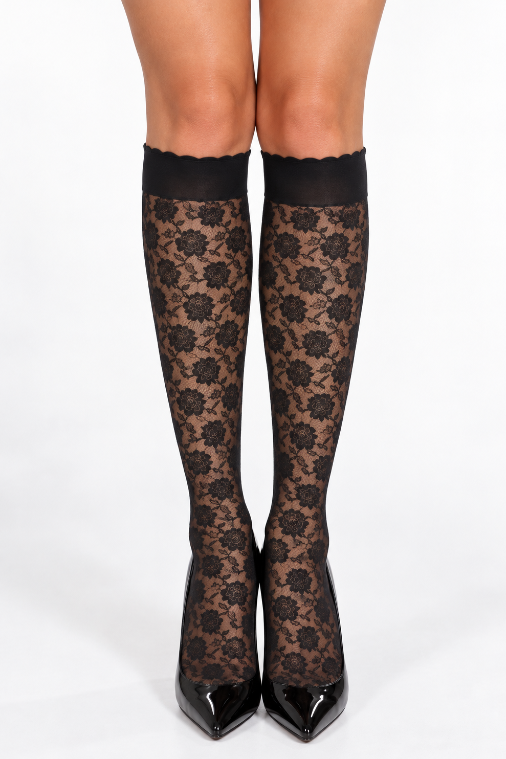 Black lace knee-high stockings with a floral pattern and solid black cuffs, worn with black pointed-toe heels against a white studio background.