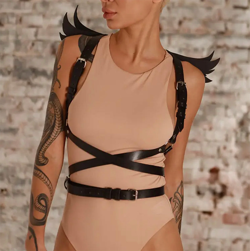 Person wearing a bodysuit with black leather harness with wings against a brick wall.