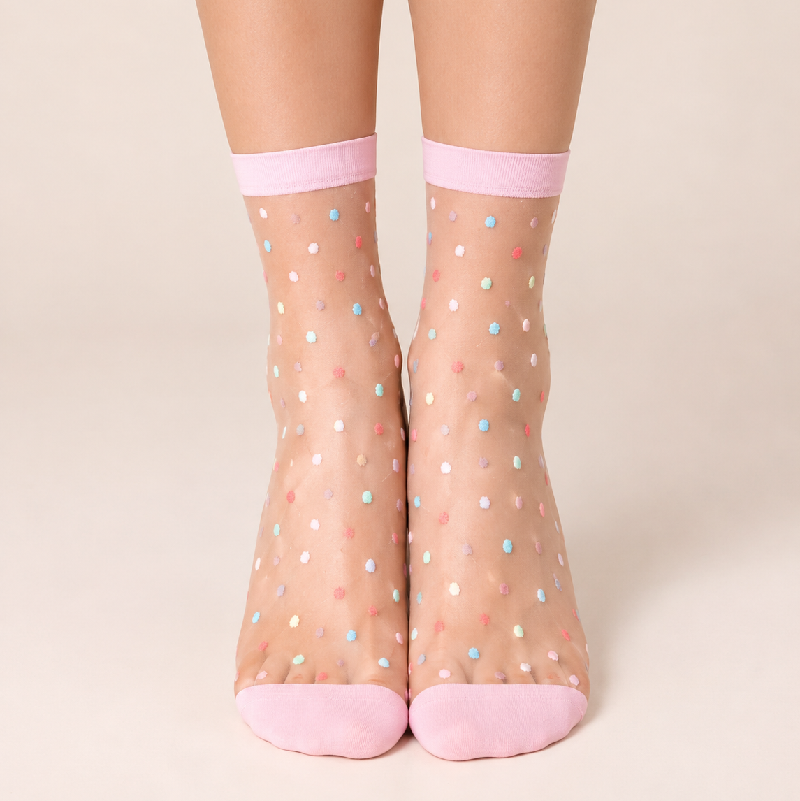 A pair of sheer ankle socks with a multicolor polka dot pattern and solid pink toes and cuffs, shown on a model's feet against a light beige background.