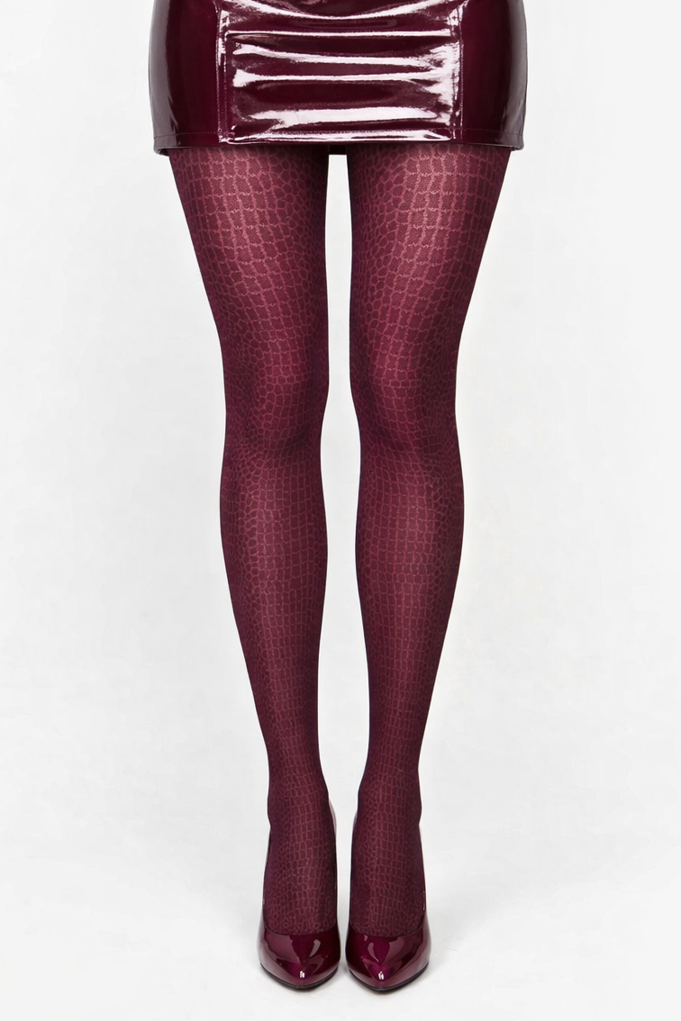 Front-facing view of a model shown from the waist down wearing a glossy burgundy vinyl mini skirt, burgundy crocodile-patterned tights, and black patent high-heeled pumps, posed with one leg slightly crossed in front against a plain white background.