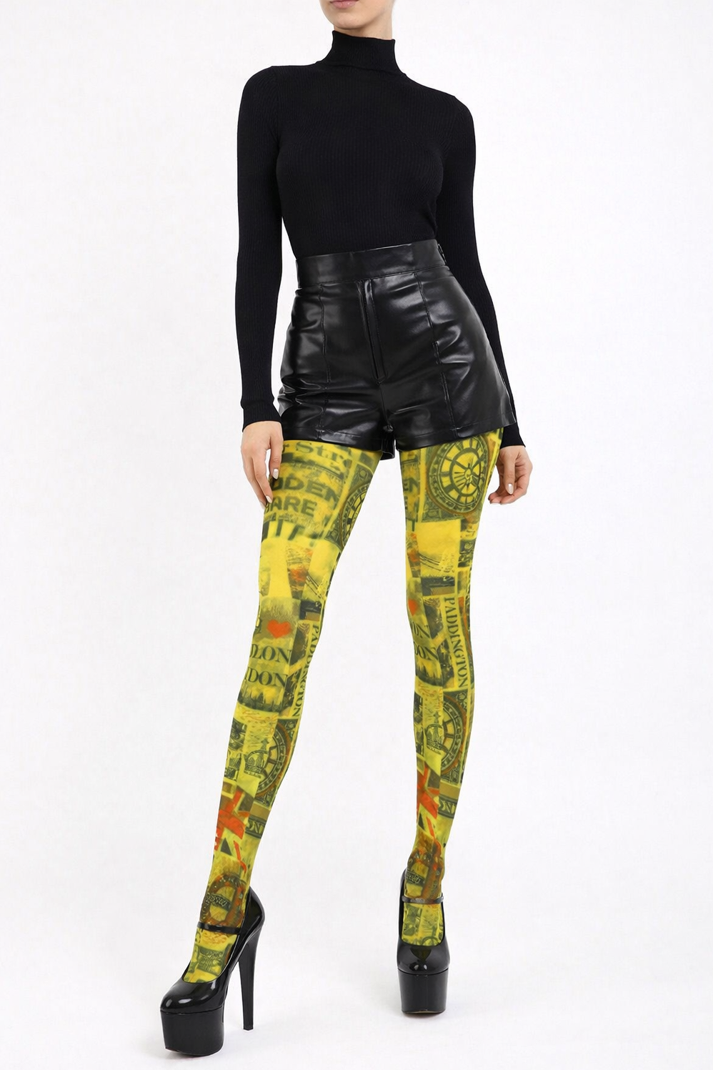 Model shown from the waist down wearing bright yellow London-print tights with legs together in a closed pose, paired with high-waisted black wet-look shorts and glossy black patent high platform heels against a plain light background.