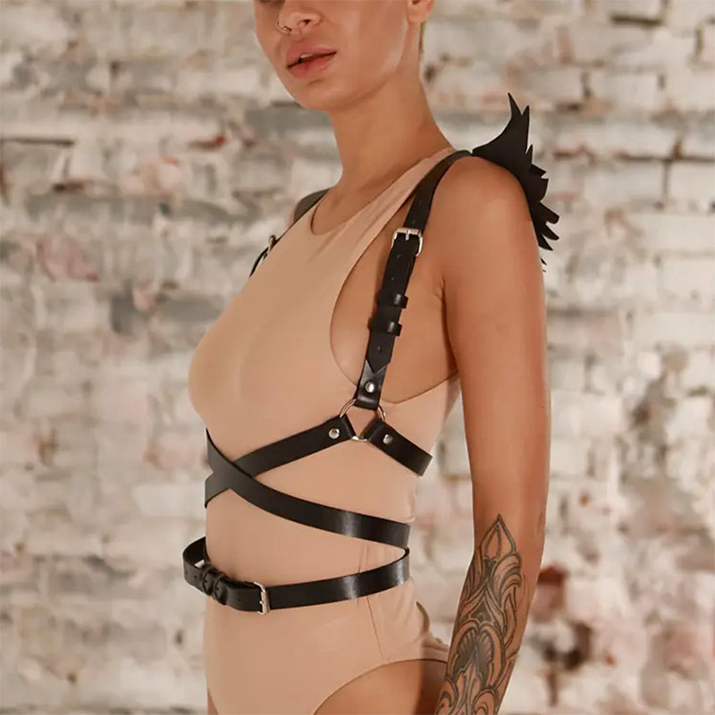 
                      
                        Person wearing a beige bodysuit with black leather straps and wings-side view against a textured wall.
                      
                    
